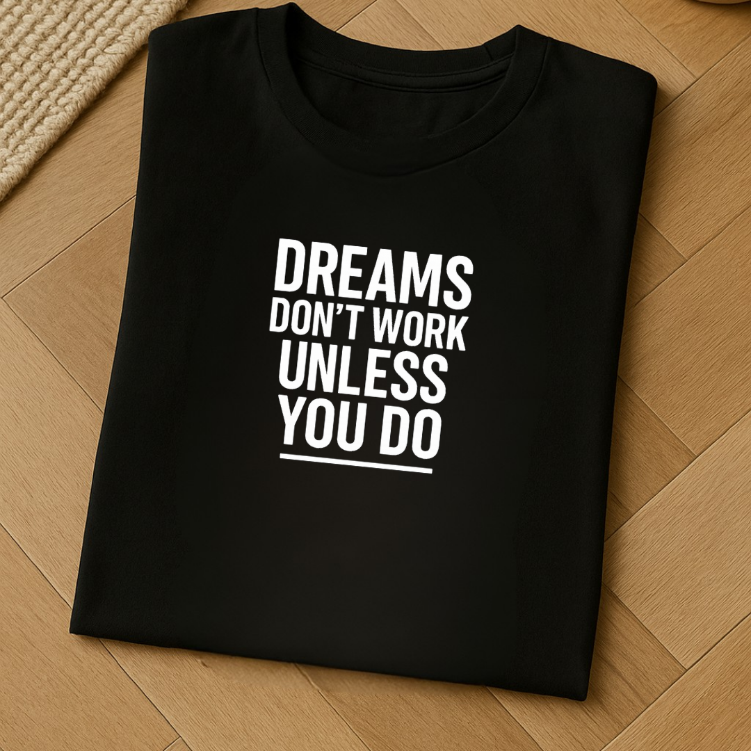 Folded black t-shirt displaying the quote Dreams Don’t Work Unless You Do on wooden floor background
