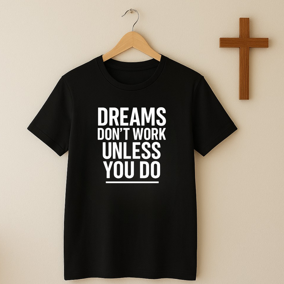 Black t-shirt hanging on wall near wooden cross with Dreams Don’t Work Unless You Do message