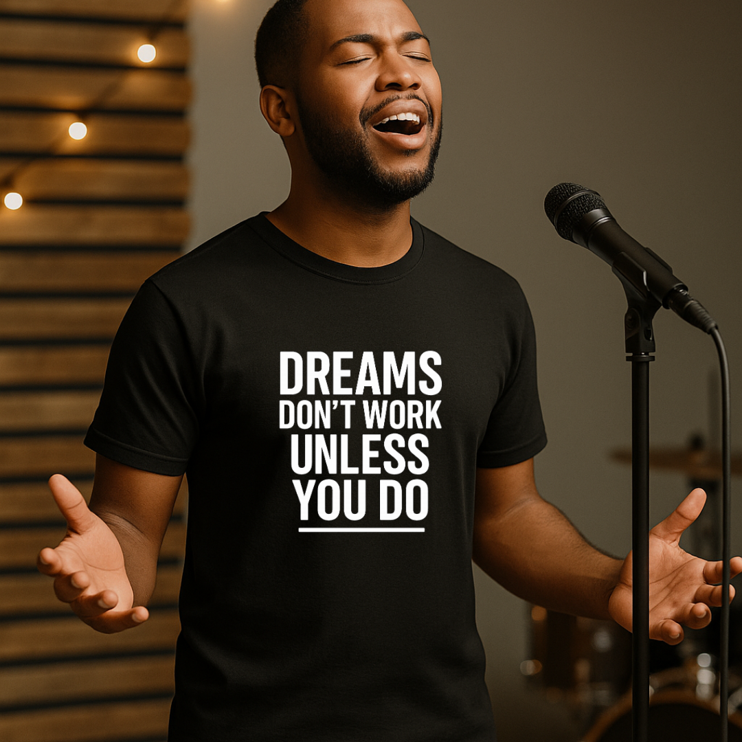 Black motivational t-shirt worn by man singing on stage with bold text Dreams Don’t Work Unless You Do