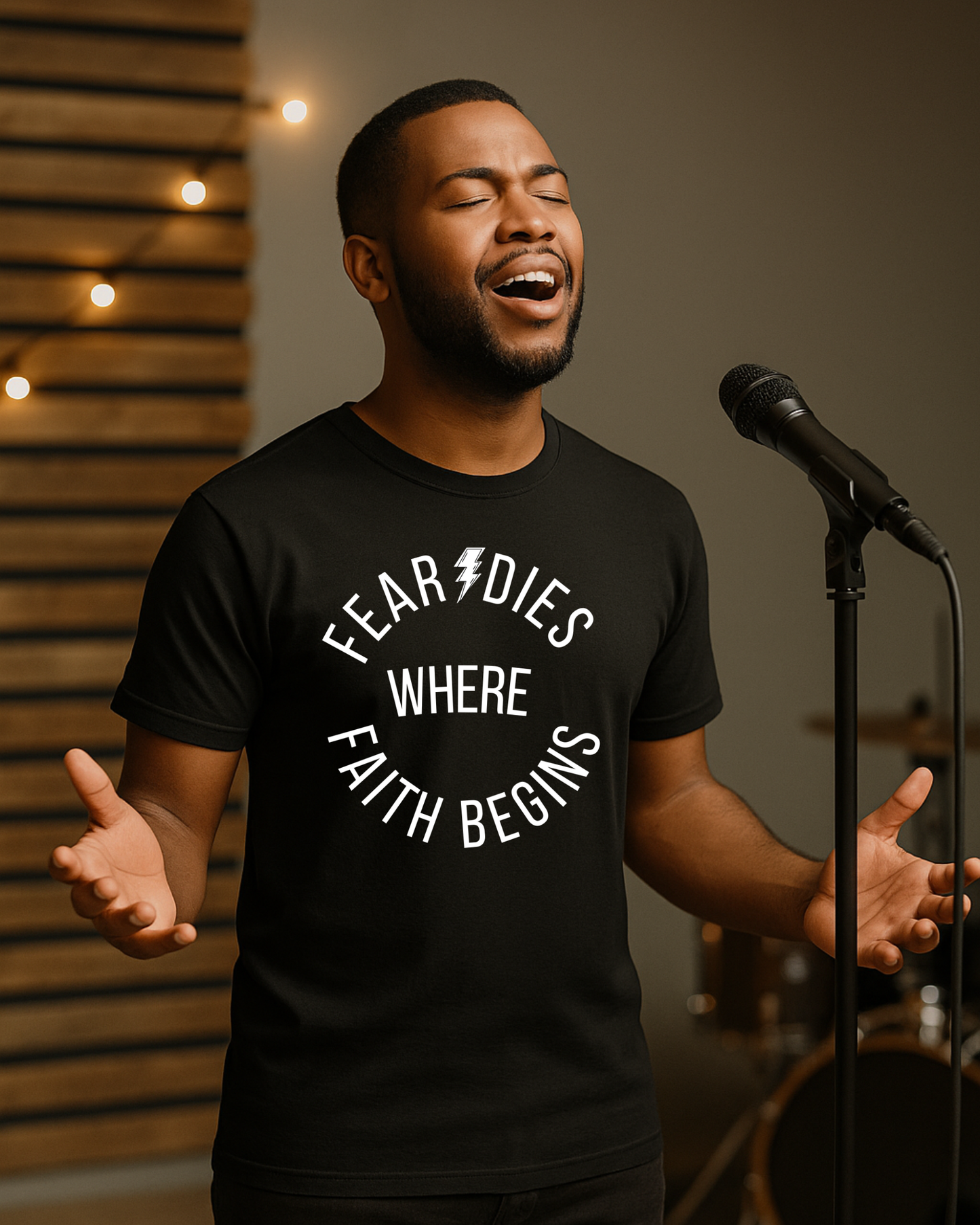 Man singing while wearing “Fear Dies Where Faith Begins” black Christian t-shirt