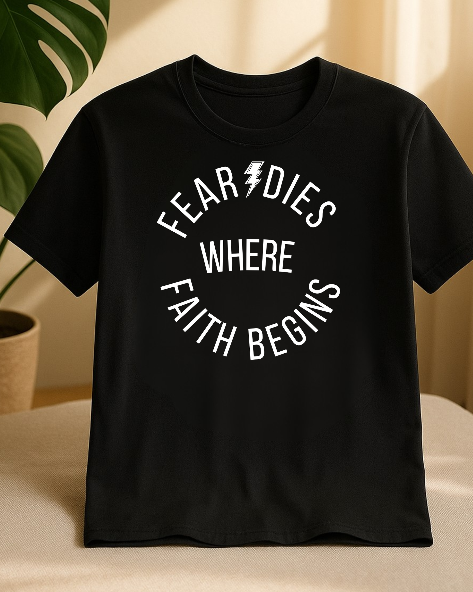 Black “Fear Dies Where Faith Begins” t-shirt displayed in soft natural light on fabric surface