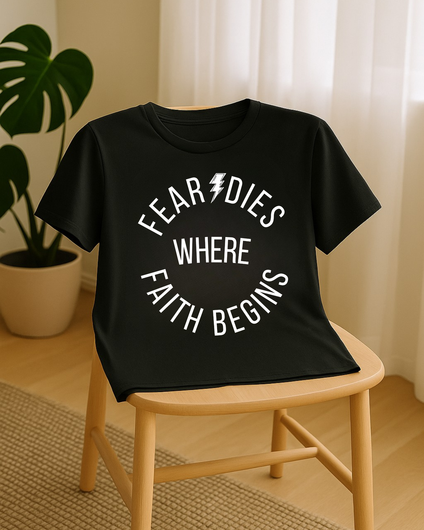 Black “Fear Dies Where Faith Begins” t-shirt displayed on chair in soft natural light