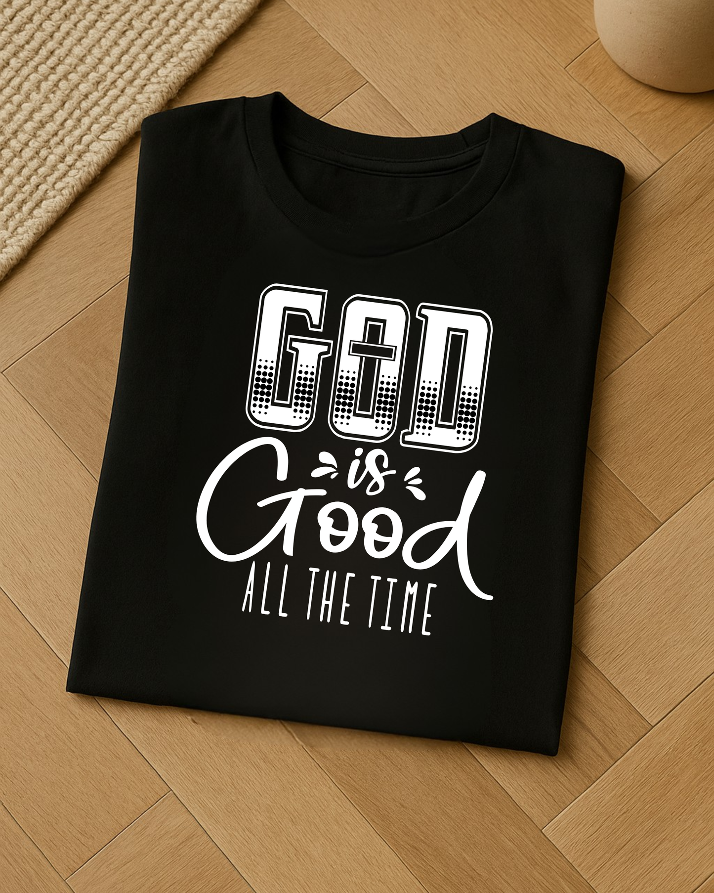Folded black Christian God Is Good All The Time t-shirt displayed on a light wood floor.