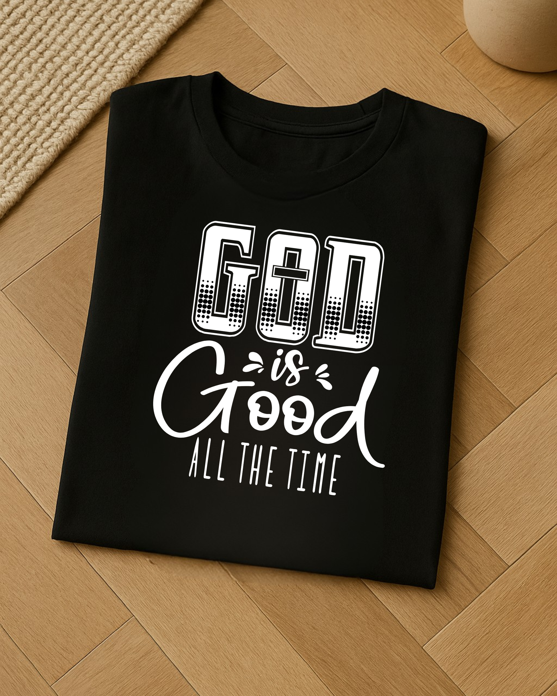 Folded black Christian God Is Good All The Time t-shirt displayed on a light wood floor.