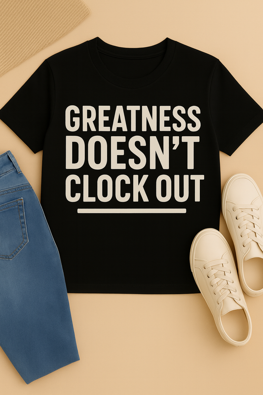 Black t-shirt with 'Greatness Doesn't Clock Out' text, paired with blue jeans and white sneakers on a beige background.