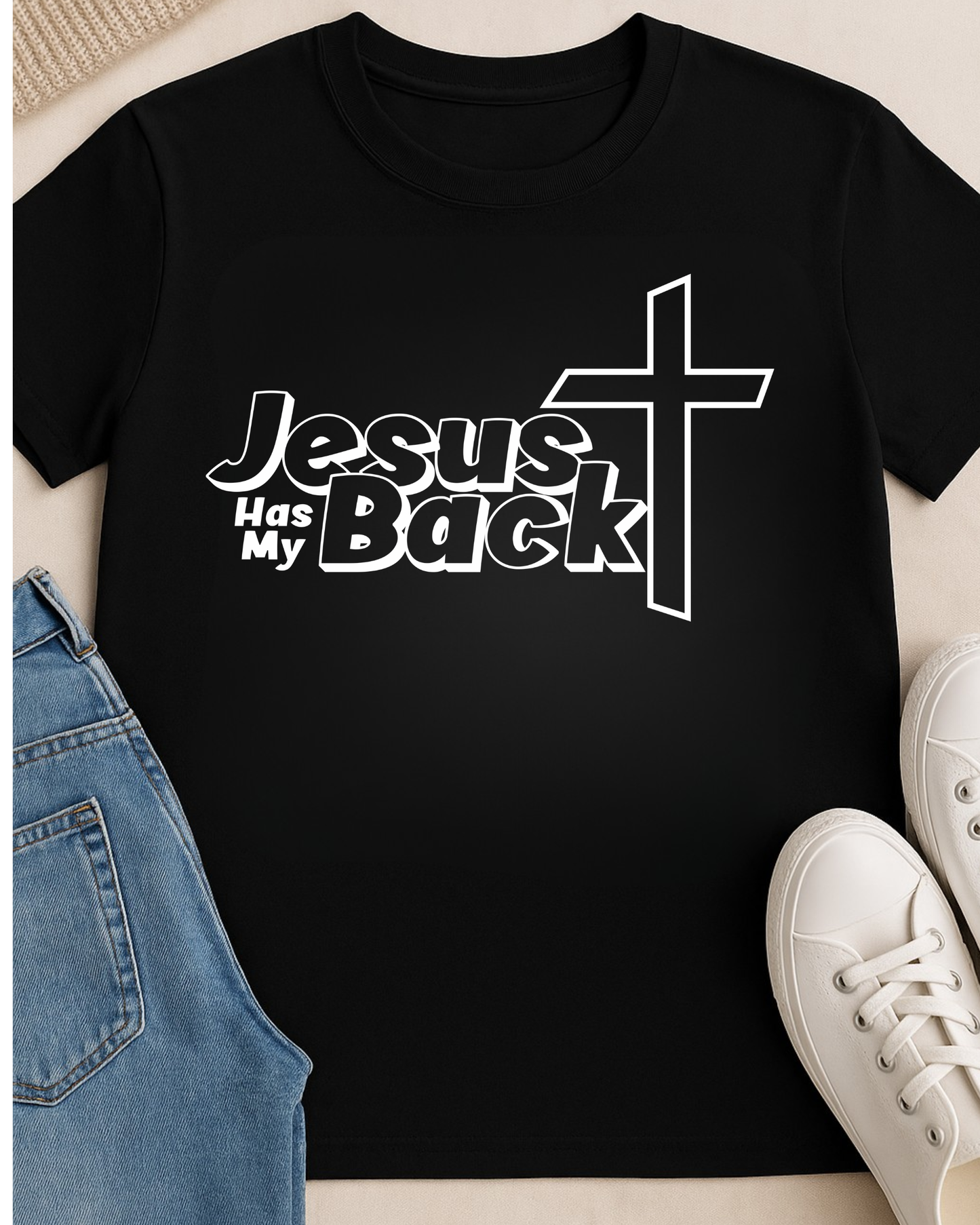 Flat lay of black “Jesus Has My Back” Christian T-shirt with jeans and shoes