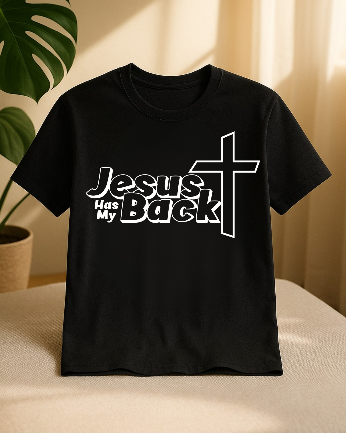 Black “Jesus Has My Back” Christian T-shirt hanging in warm indoor light with plant