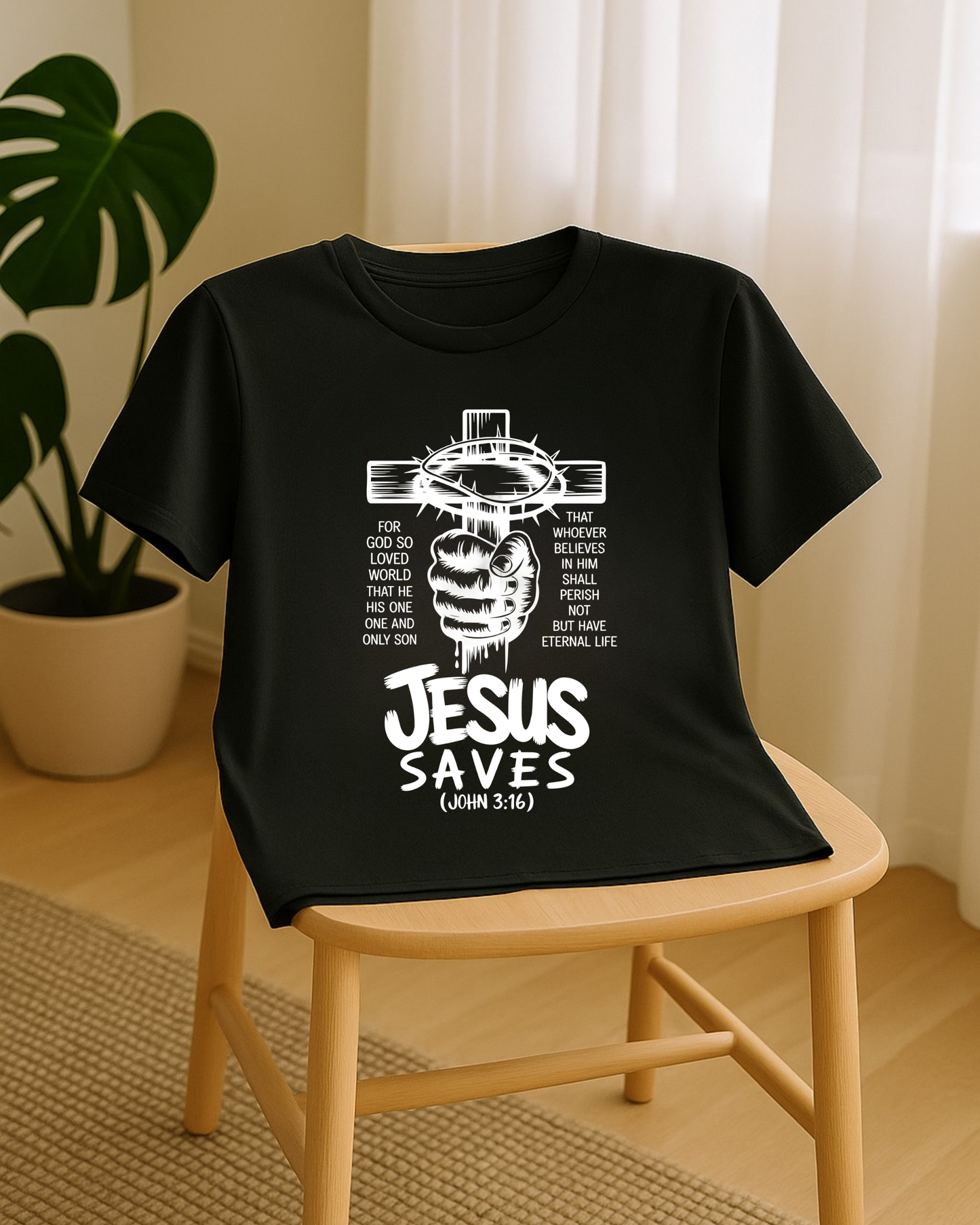 Black Christian T-shirt with Jesus Saves John 3:16 cross design displayed on a wooden chair in a bright room.