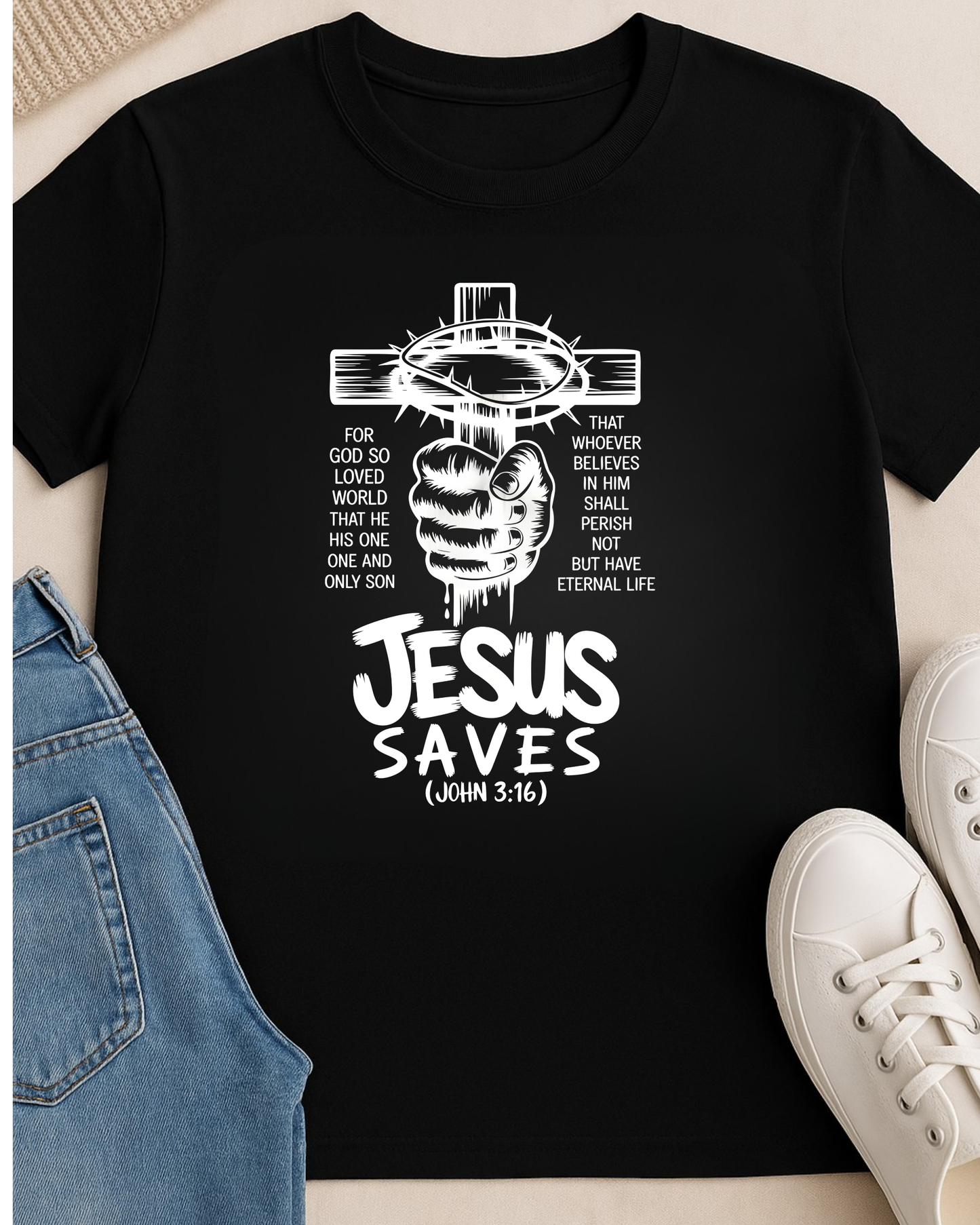 Flat lay of a black Christian T-shirt featuring a “Jesus Saves John 3:16” cross design styled with jeans and white sneakers.