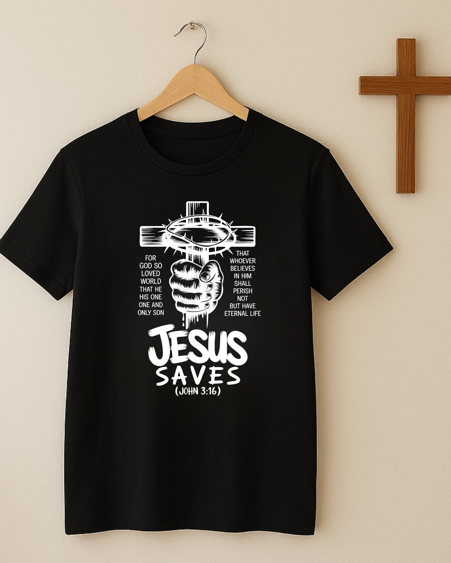 Black Christian T-shirt hanging on a wooden hanger with a “Jesus Saves John 3:16” cross design displayed beside a wall cross.