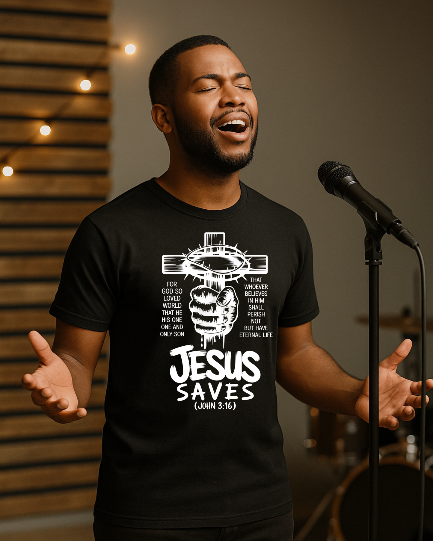 Man singing on stage wearing a black Christian T-shirt that reads Jesus Saves John 3:16 with a cross design.