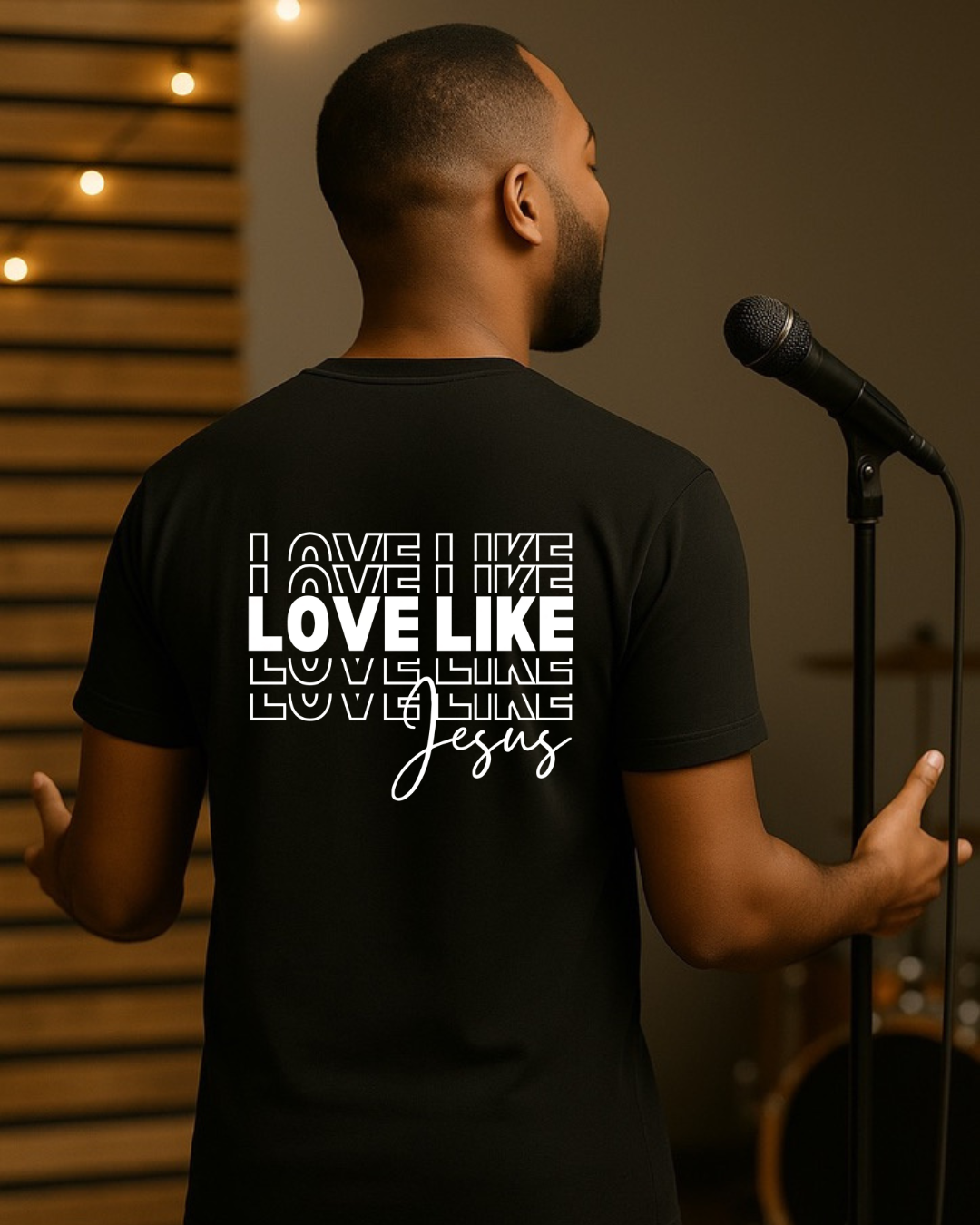 Man wearing black “Love Like Jesus” Christian T-shirt in a stage setting, faith-based inspirational apparel