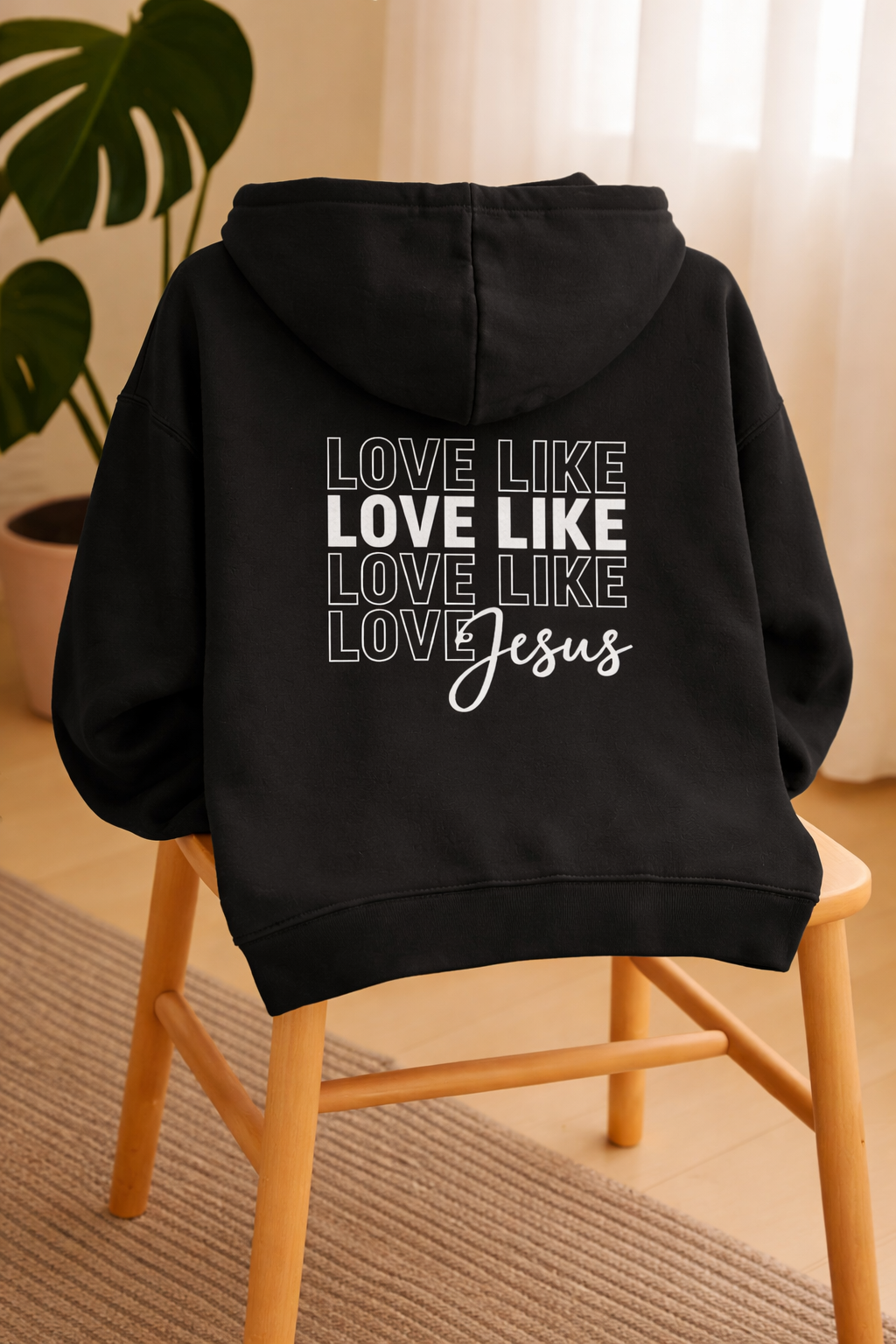 Black Love Like Jesus hoodie displayed on chair in home setting