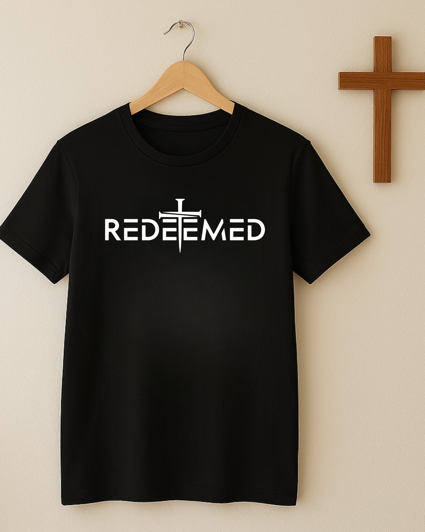 Black Christian REDEEMED t-shirt on hanger against beige wall with wooden cross.