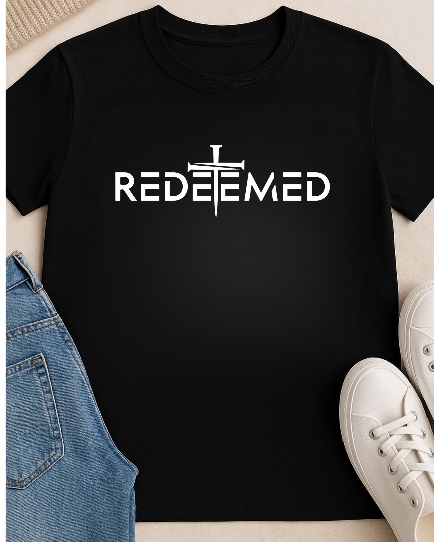 Black t-shirt with ‘REDEEMED’ text on a neutral background with pants and shoe