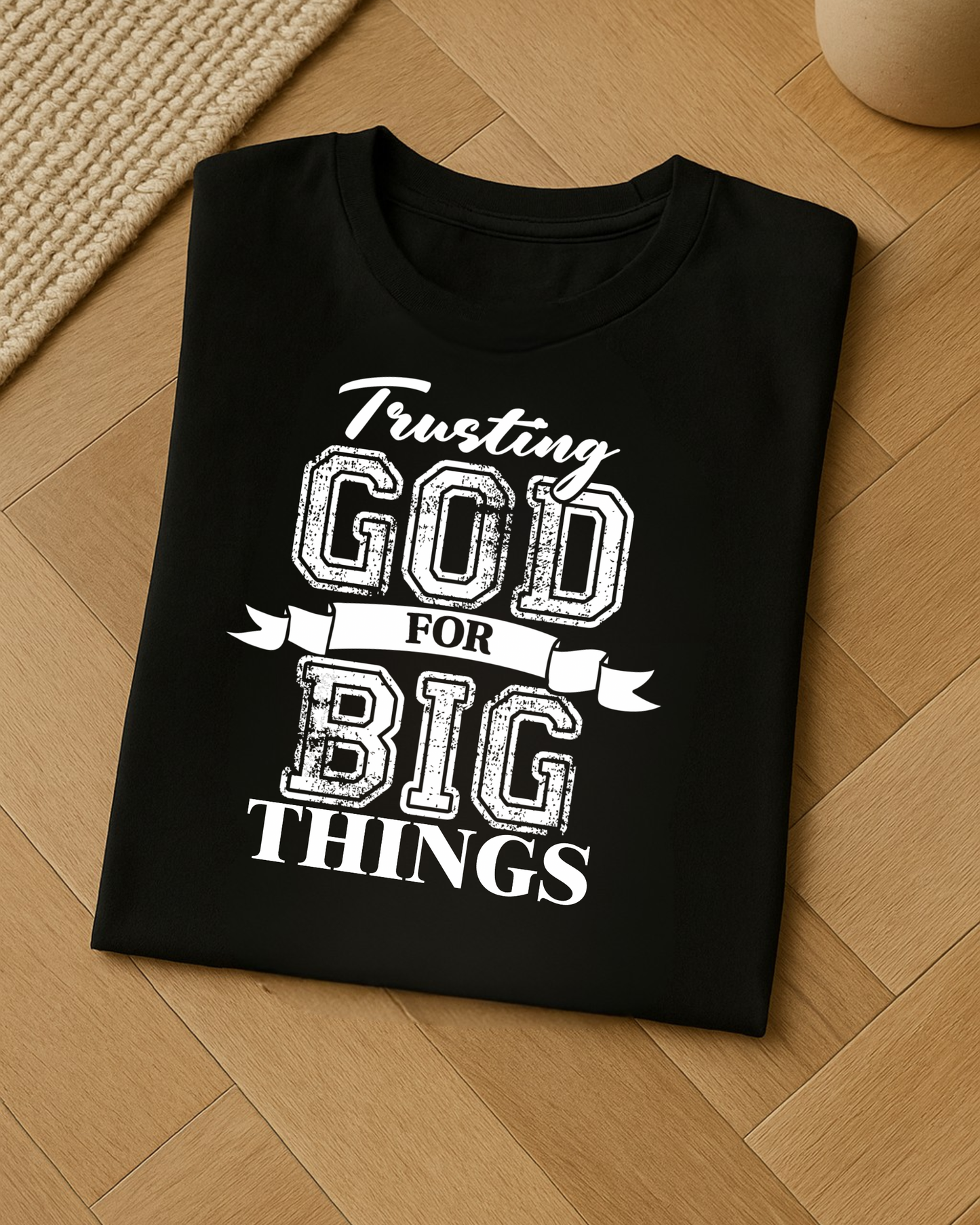 Folded faith-based t-shirt on wooden floor showcasing trusting God for big things saying