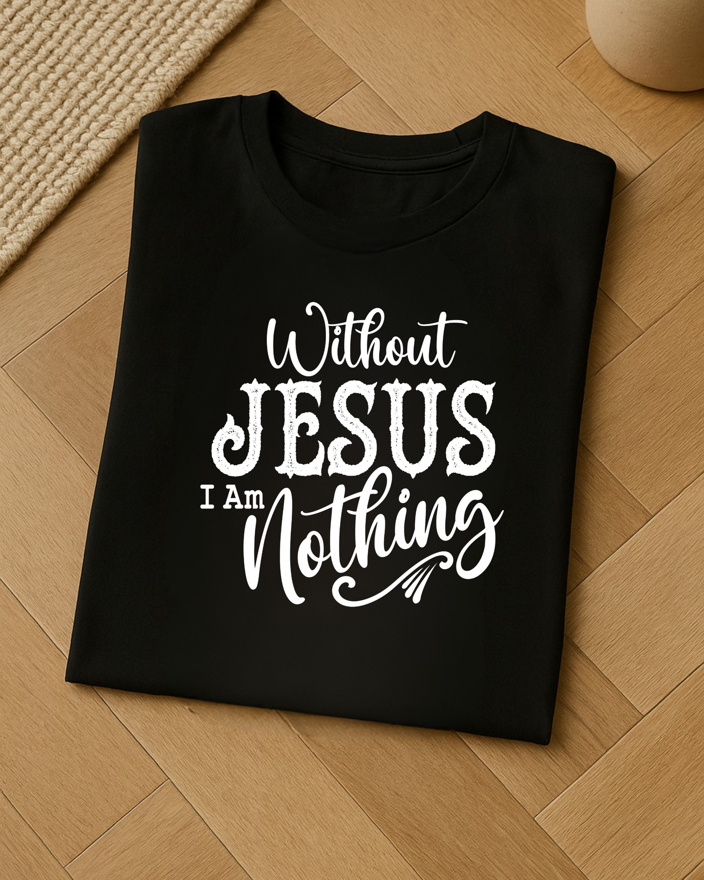 Folded black Christian T-shirt on wooden floor featuring the quote “Without Jesus I Am Nothing” in bold white lettering.